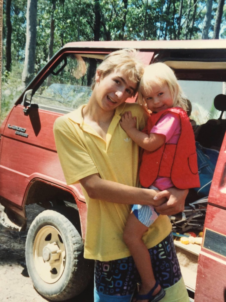 Gordon as a teenager in the bush holding his little sister, beside a red four-wheel-drive
