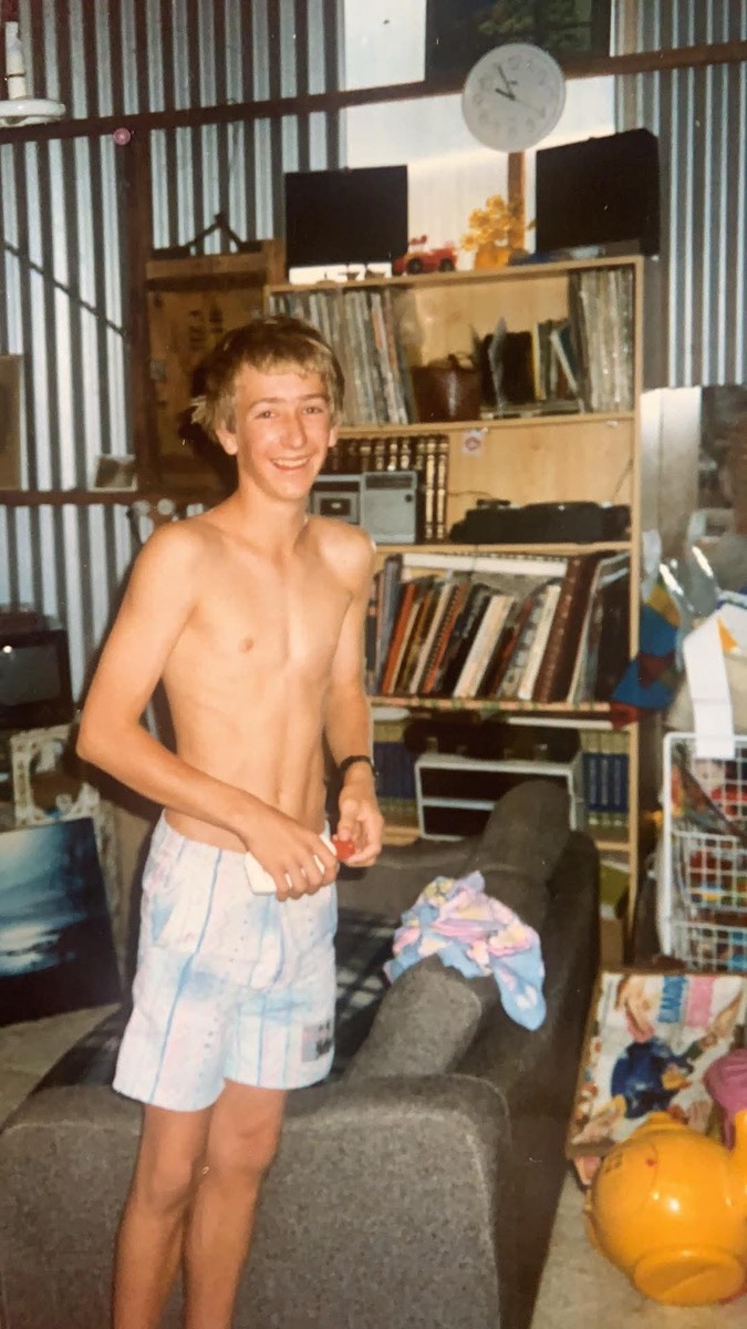Gordon as a teenager grinning in a shed lined with shelves of records and books